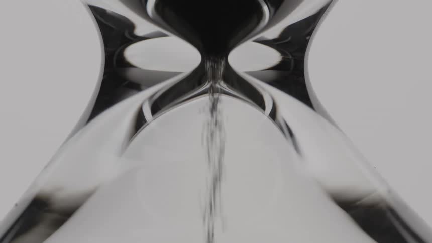Sand falling inside of an hourglass next to a white wall