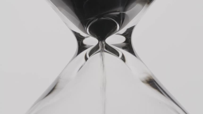 A close up of black sand falling through an hourglass