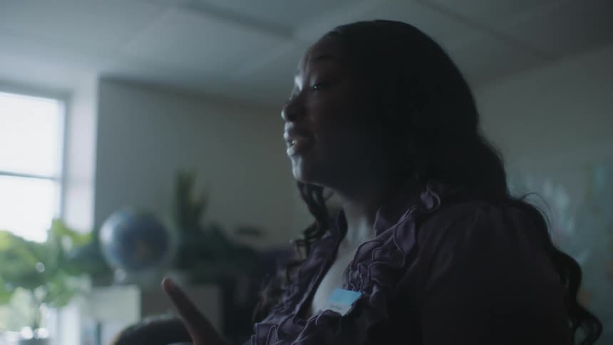 Woman stands in room giving a talk with globe on cabinet near window