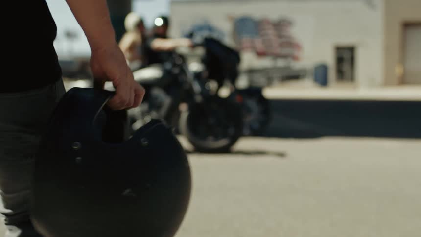 White man holding a helmet walking towards a motorcycle parked next to a couple boarded on another motorcycle