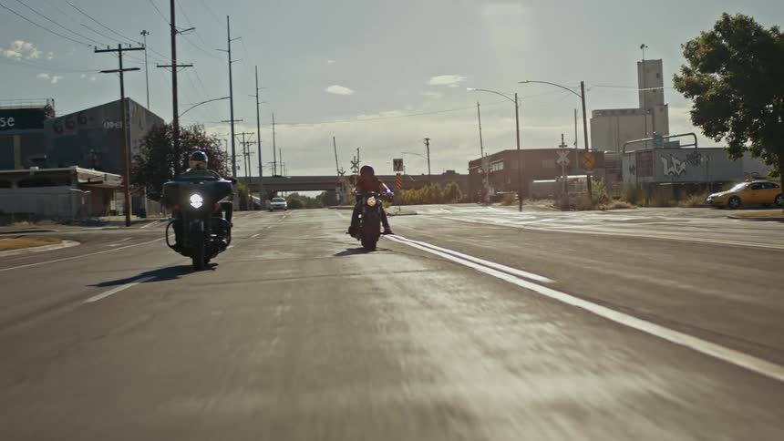 A pair of motorcyclists travel down a city street during the day