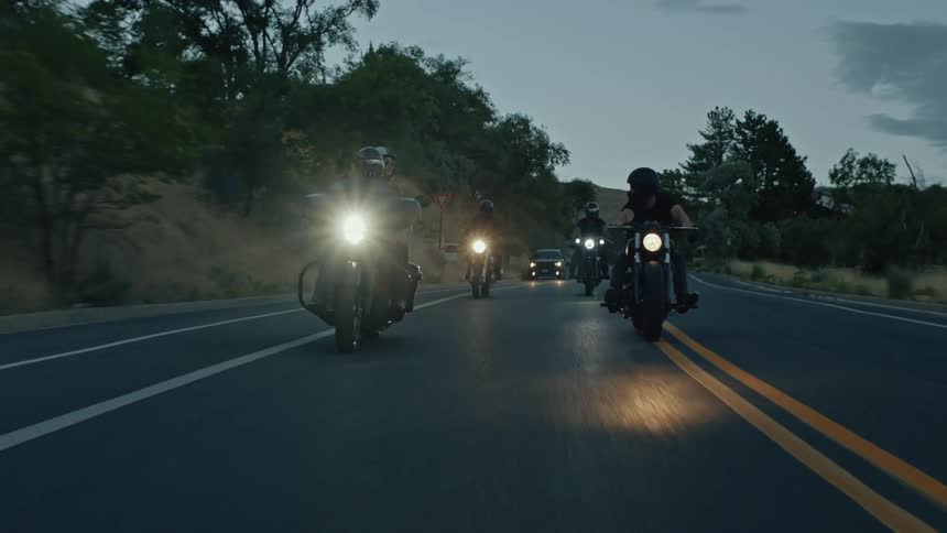A group of bikers drive down a country road in the evening