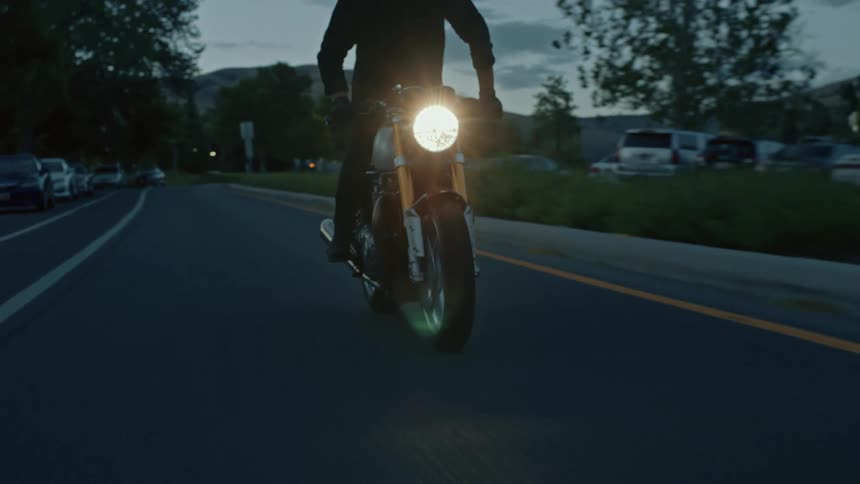 Man riding a motorcycle on a highway with the headlight on at dusk as he weaves in and out