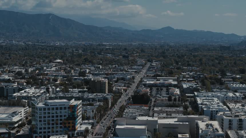 Drone view of a city split by a highway winding towards the mountains in the distance
