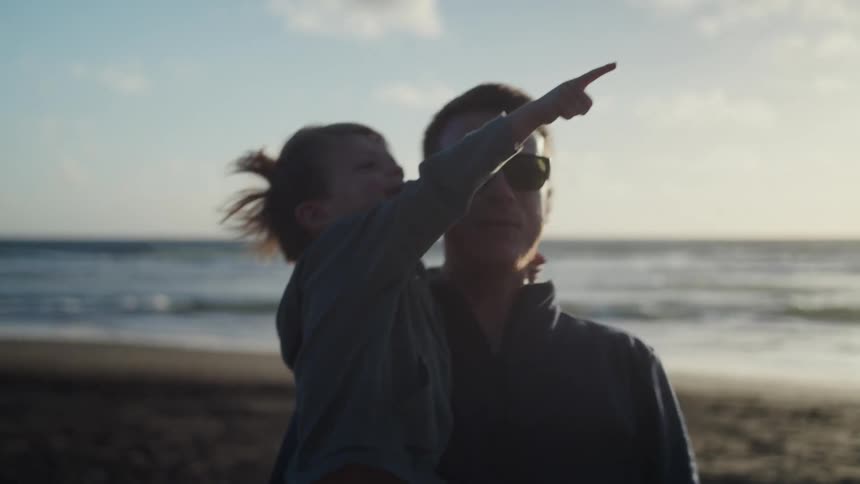 A father holds his son in the shade on the beach as they both point in the air