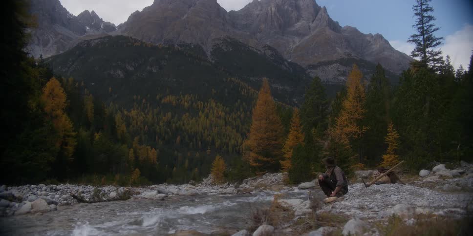 A man is sitting next to a river in the wilderness
