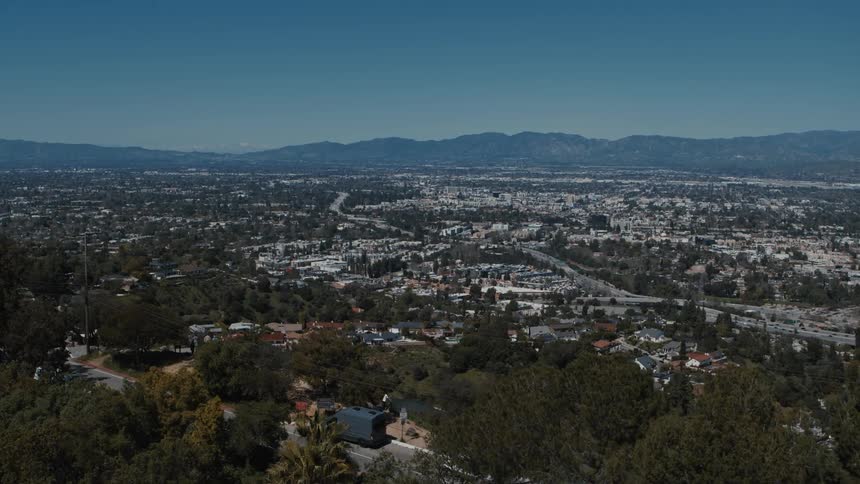 Palm Trees and Mulholland drive frame an establishing shot of the Valley and the 101 Freeway in Los Angeles