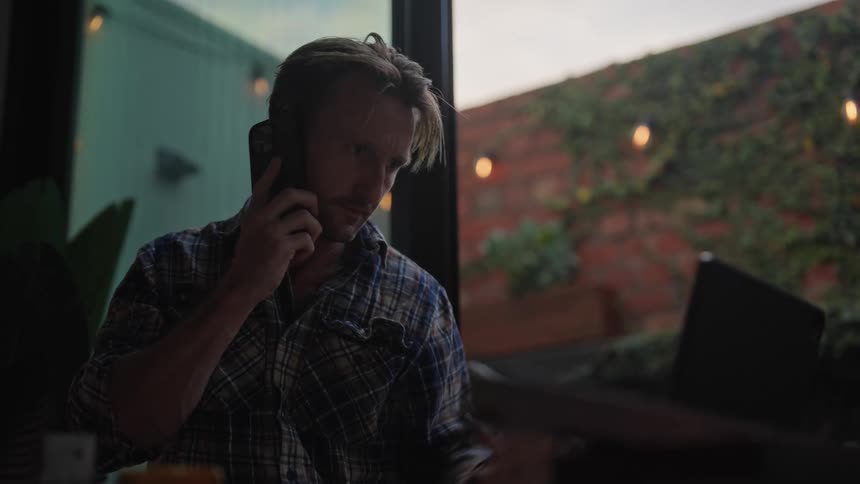 White male talking on a phone and grabbing a pen off the top of a computer screen