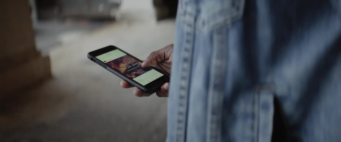 Person in jean jacket scrolls on cell phone