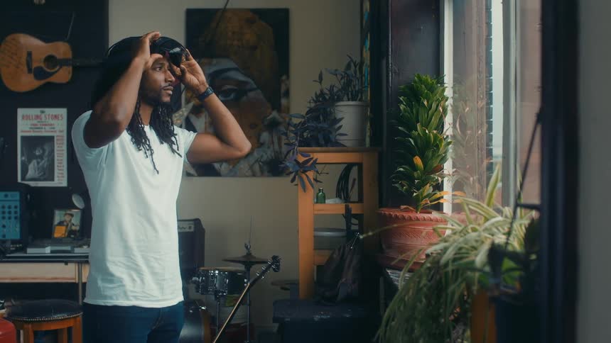 Man standing in a room with plants and instruments putting on a virtual headset and goggles