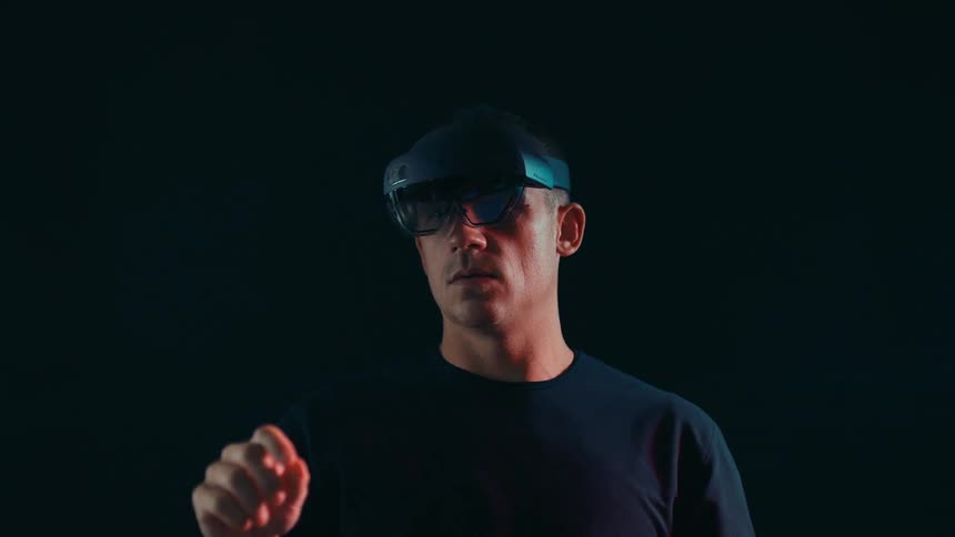 Man standing in a black room wearing a virtual headset moving his arms around in creative motions