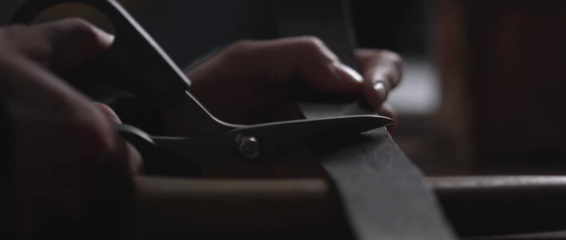 A woman uses scissors to cut a piece of leather