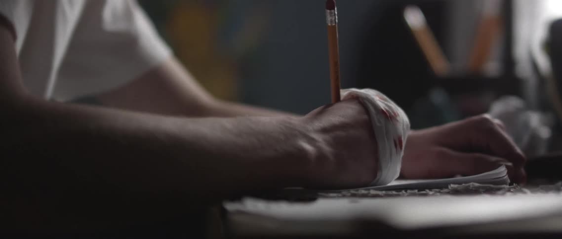 A young man sits in a class and writes with a bandaged up hand