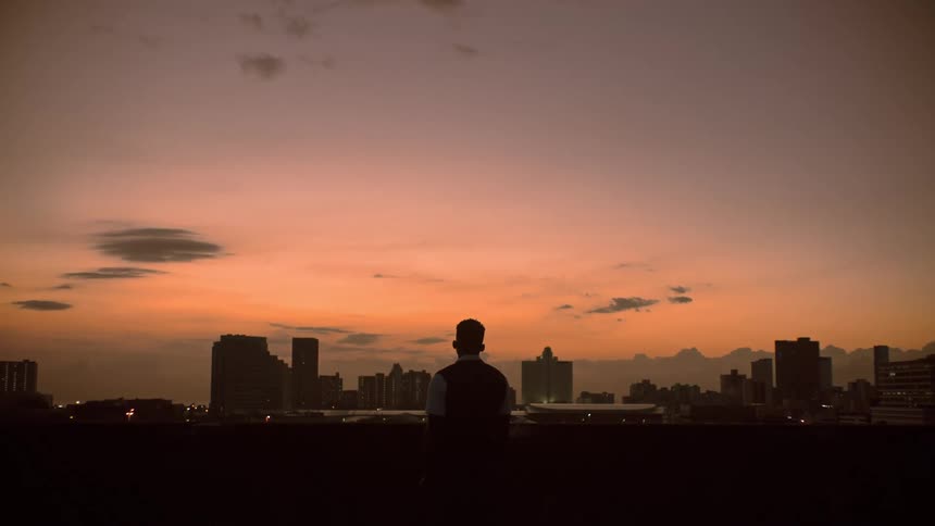 Man facing away looking at the horizon and buildings from the rooftop during sunset