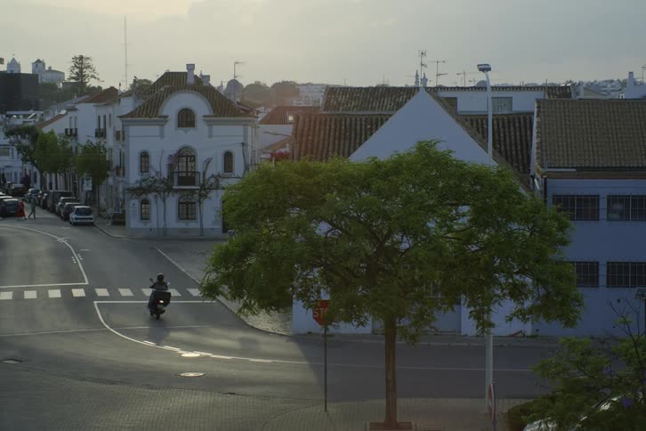 A wide shot of a person on a motorcycle driving down t he road near houses in a village