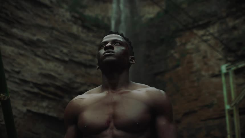 Portrait of an African man standing without a shirt on looking around him with a waterfall behind him