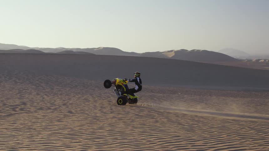 A man does a wheelie in the desert on his four wheeler