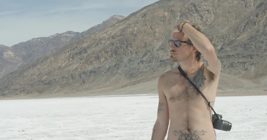 A shirtless man in sunglasses wipes his forehead