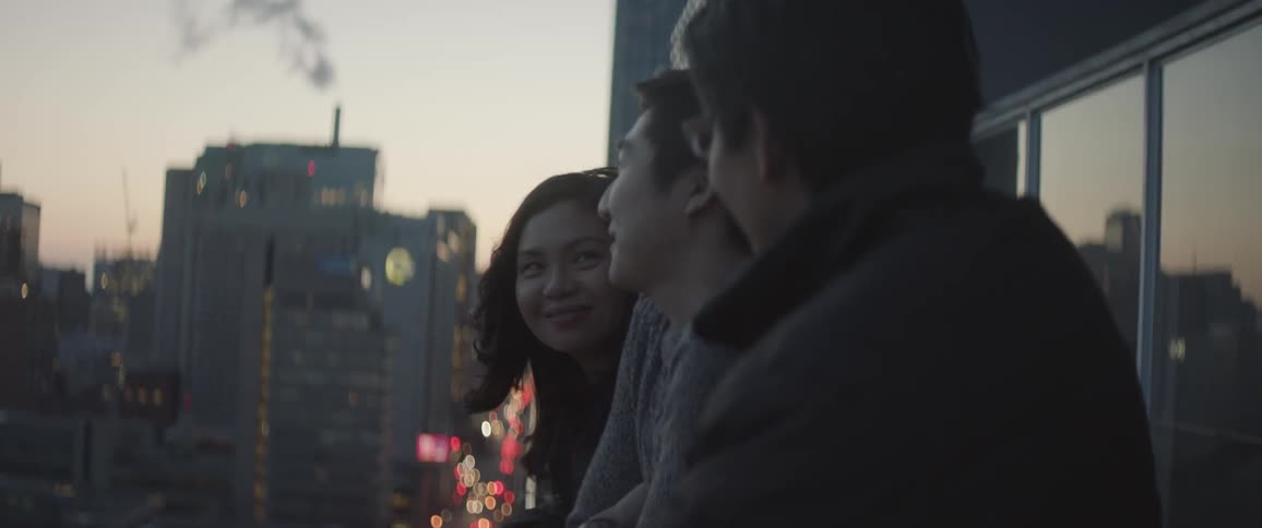 Three people talk while looking over the railing towards a city