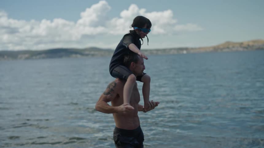 Man carrying his daughter on his shoulder coming out of the water at the beach