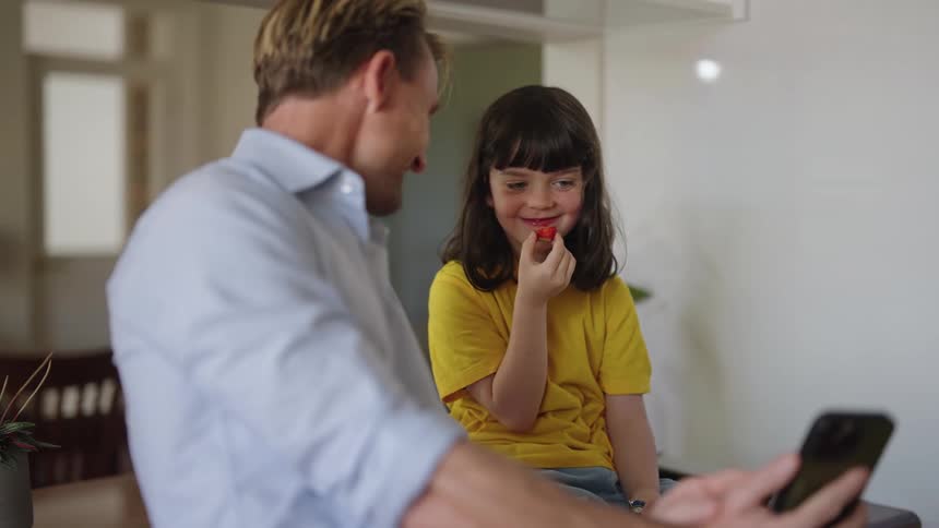 Daughter eats while she and father watch smartphone screen