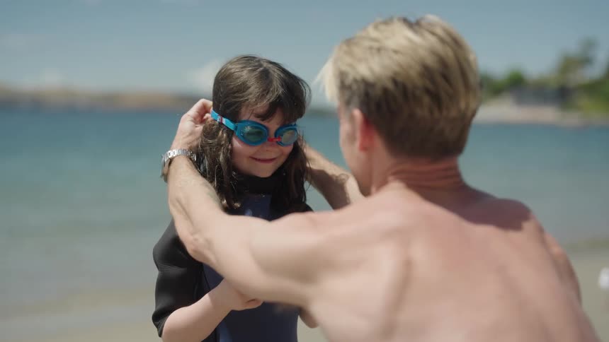 Father and daughter high five after he fixes her goggles then the girl runs across beach toward water