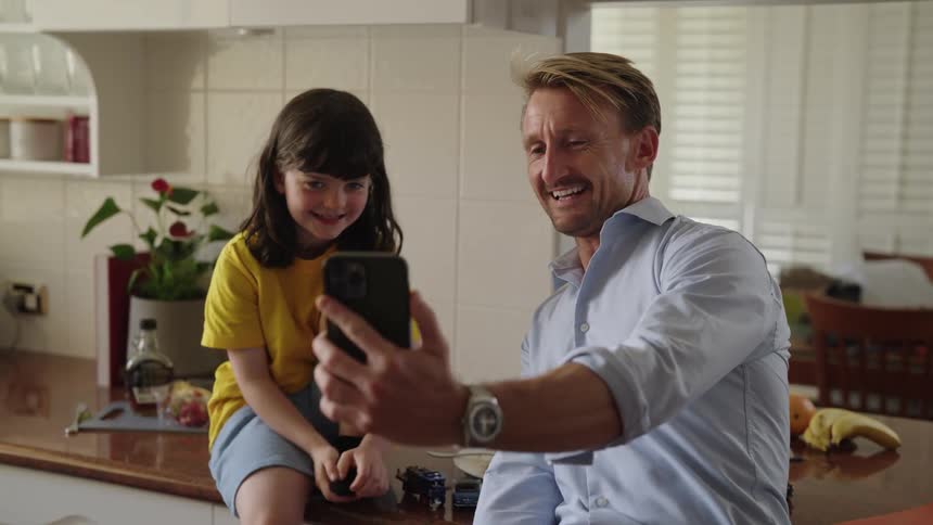Daughter sits on kitchen counter as he and daughter wave during video call