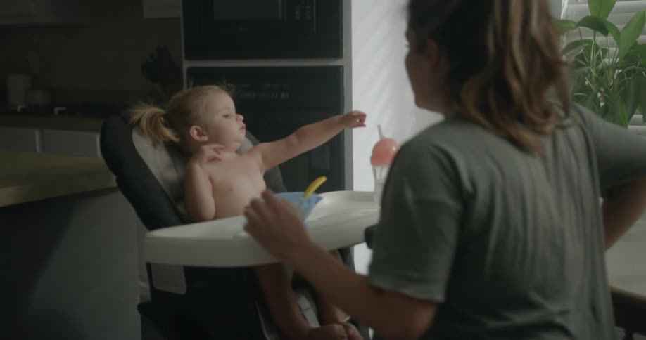 Mother sits down near high chair to feed daughter