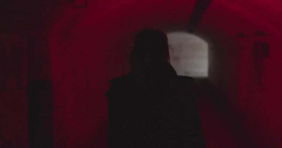 A woman walks down a tunnel lit with a red flash light