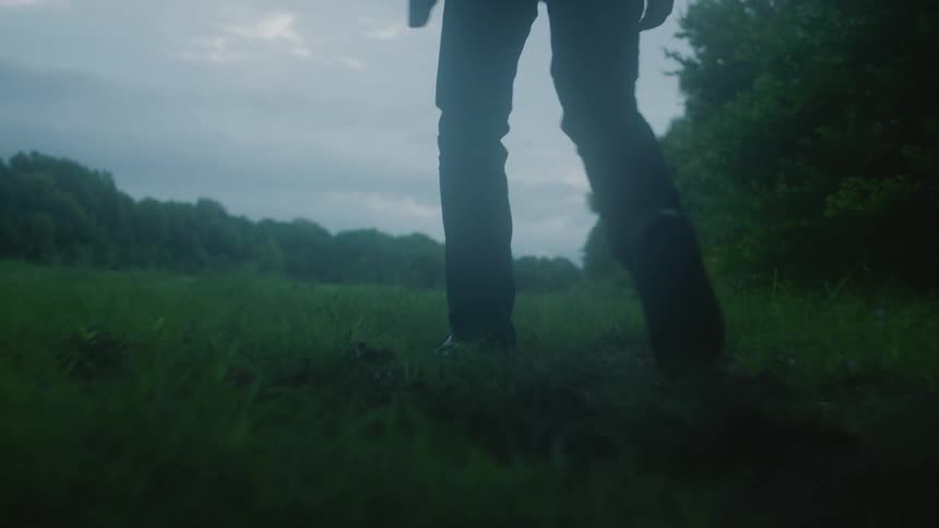 A man is walking over the field on a cloudy day