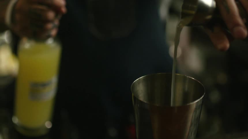 A bartender pours a liquid into a jigger and then into a mixing tin
