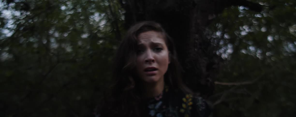 A woman looks scared while standing in front of a tree