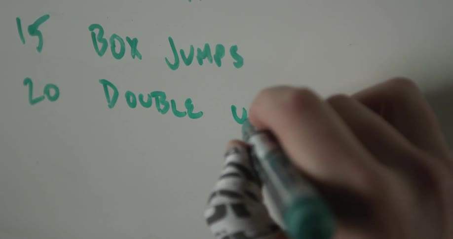 A hand writes a fitness routine on a whiteboard