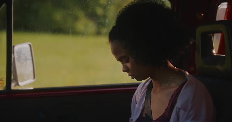 Downcast female passenger sits in vehicle parked near field