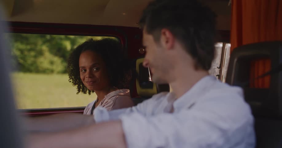 Female passenger frowns then smiles at driver as they park in caravan near field