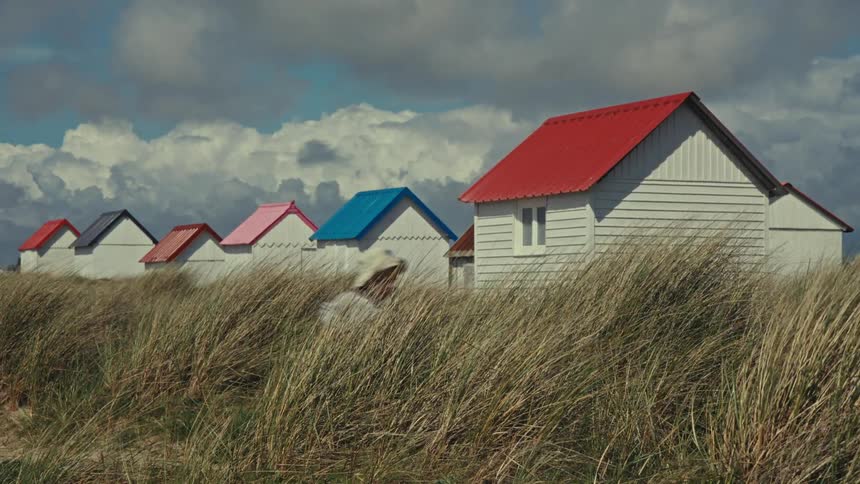 Young boy runs near the tall grass growing behind houses with colorful roofs in the countryside