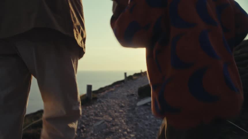 Young child holding mothers hand walking along the sea