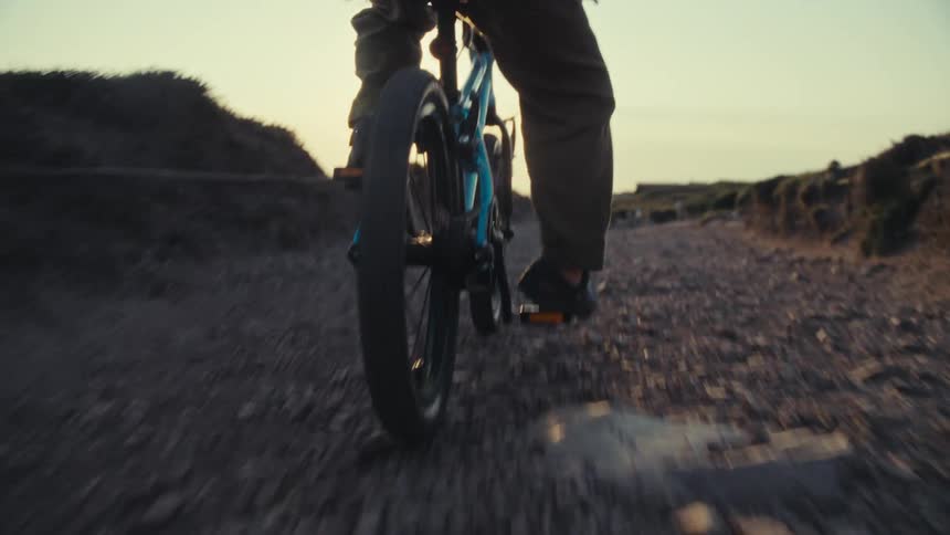 Child rides a bike on a rocky path by the ocean