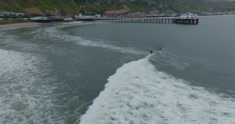 A surfer rides a wave towards Malibu Pier