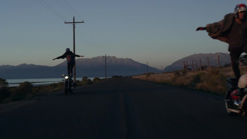 A man is doing a trick standing on his moving motorcycle
