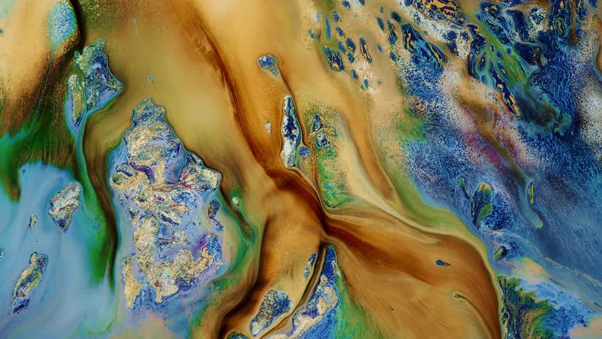 Yellow and brown liquid flows across a colored surface stretching out in streams as colors blend and mix