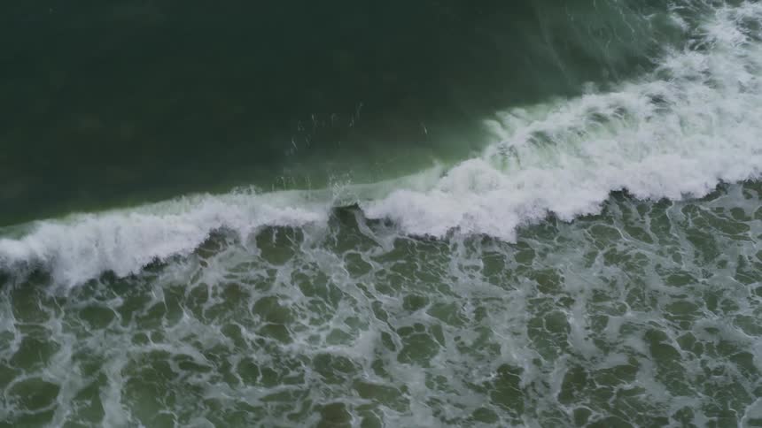 An aerial view of a sea wave rolling toward the shore
