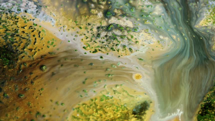 Water and paint flowing and blending with each other over a textured surface with golden particles