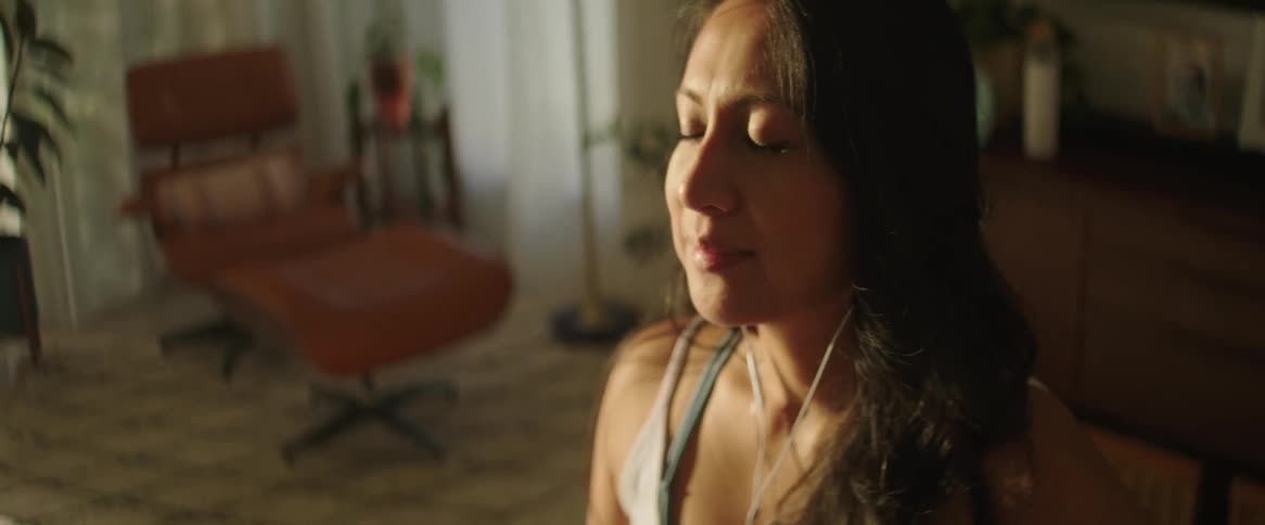 A close up of a woman sitting with her eyes closed wearing headphones in her living room