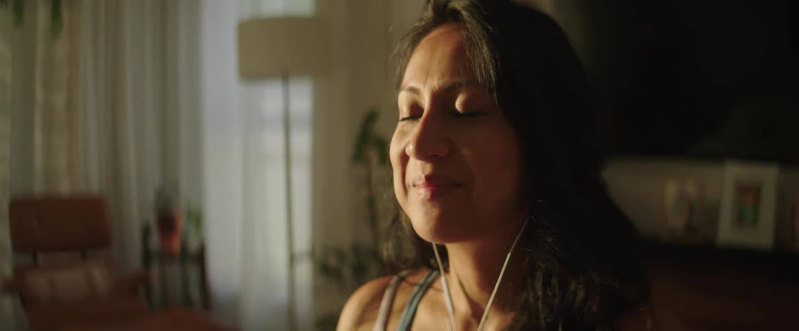 A close up of a woman sitting with her eyes closed and headphones in beathing and smiling