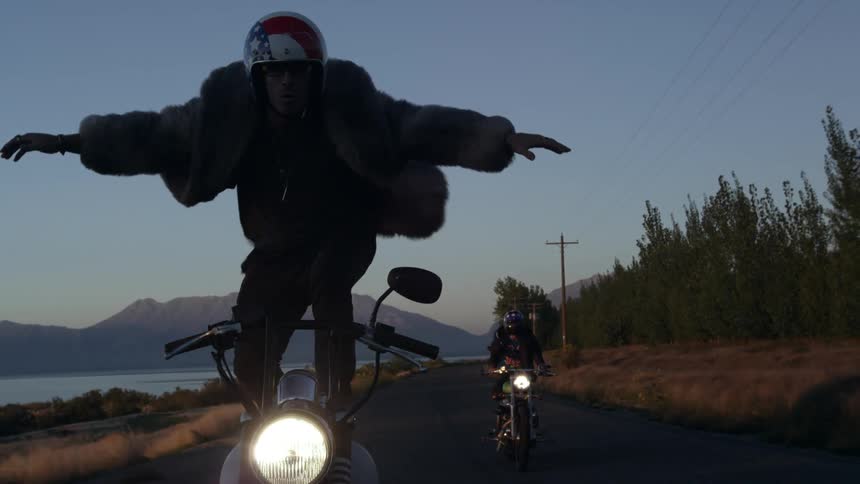 A man stands up on his motorcycle while he drive sit