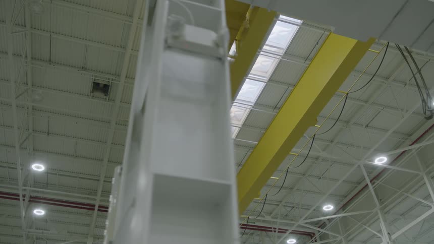 The ceiling of a large facility has large yellow support beams mounted on it
