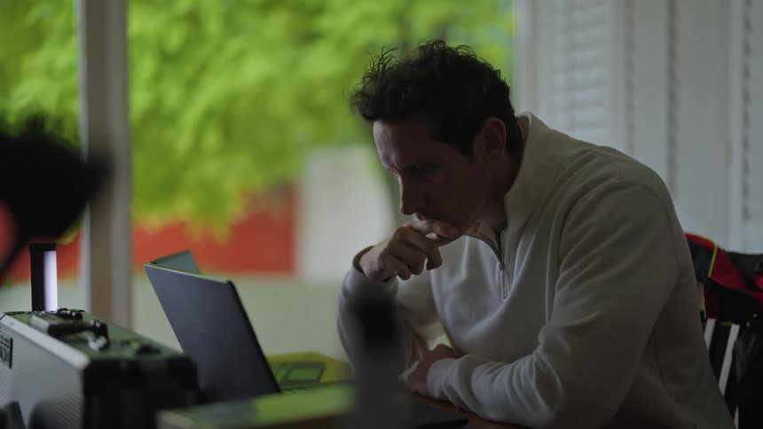 A man uses a laptop while sitting a table indoors during the day