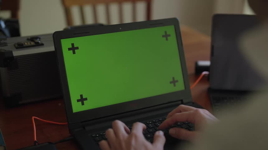 A person is typing on a laptop computer with a green screen