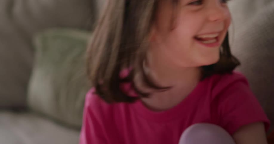 A little girl laughs while playing a video game on a sofa